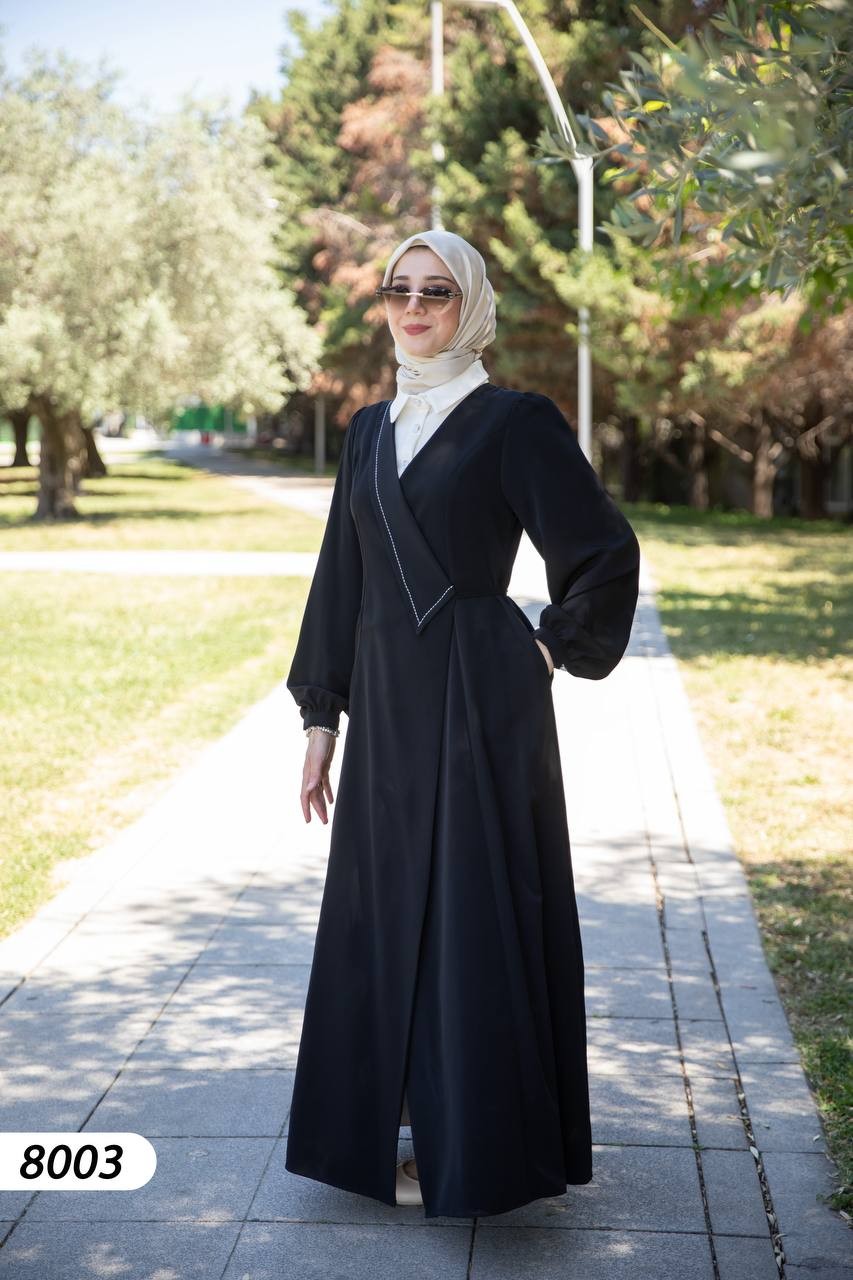 alwaan black maxi abaya dress with white collared shirt insert, wrap bodice, and long sleeves worn by a woman outdoors