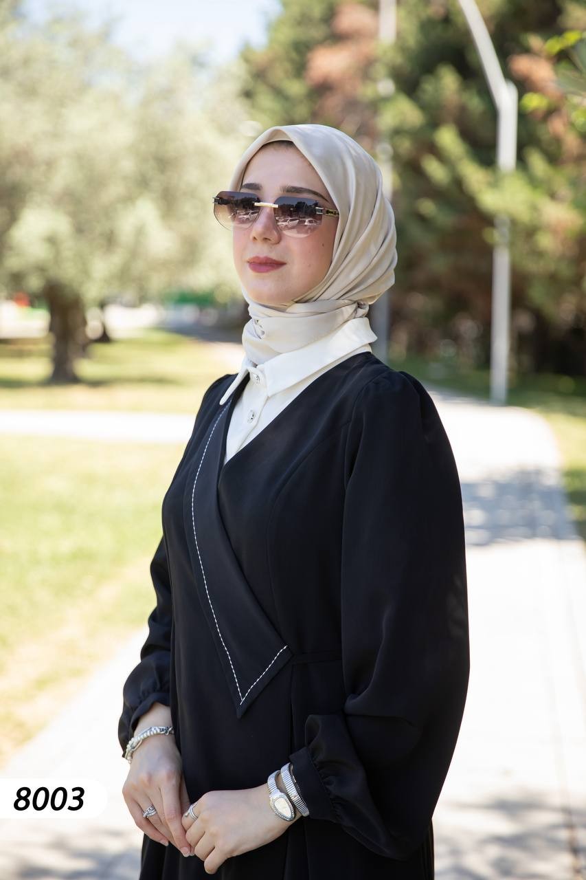 alwaan black wrap-style abaya dress with white collar and layered shirt detail worn with a beige hijab outdoors