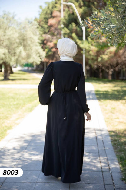 alwaan black maxi abaya dress with white collar, long sleeves, and adjustable back tie worn by a woman in a park